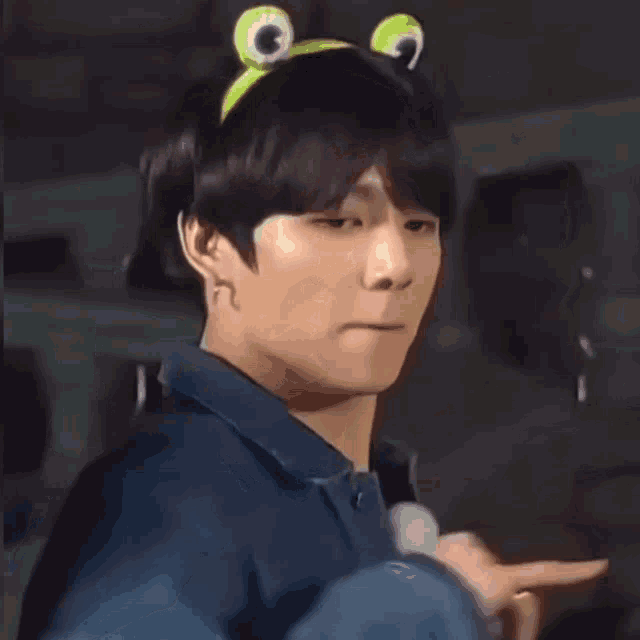 a young man wearing a frog headband is making a funny face and pointing at the camera .