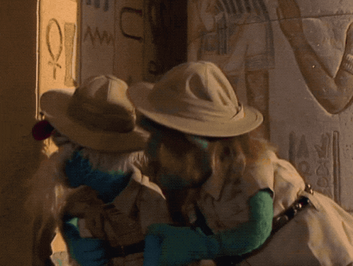 a couple of muppets standing next to each other in front of a wall that has the letter u on it
