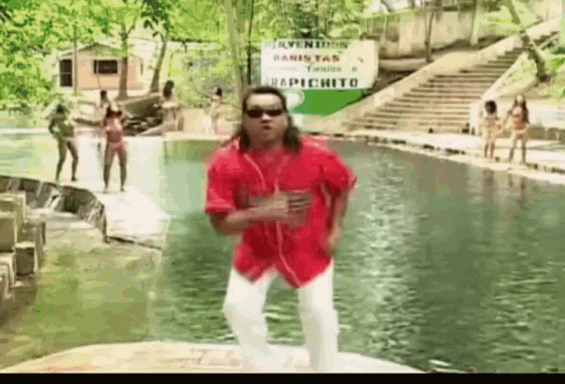 a man in a red shirt and white pants is dancing in front of a sign that says repichito