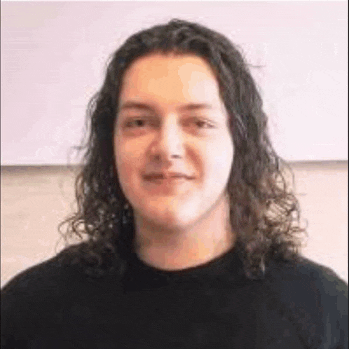 a young man with long curly hair is wearing a black sweater and smiling .