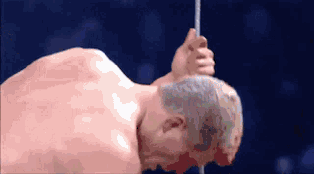a shirtless man is hanging from a pole with his head down