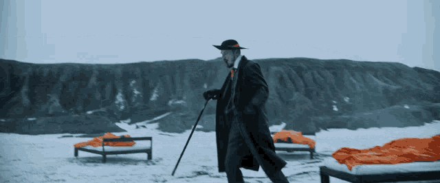 a man in a suit and hat is walking in the snow holding a cane