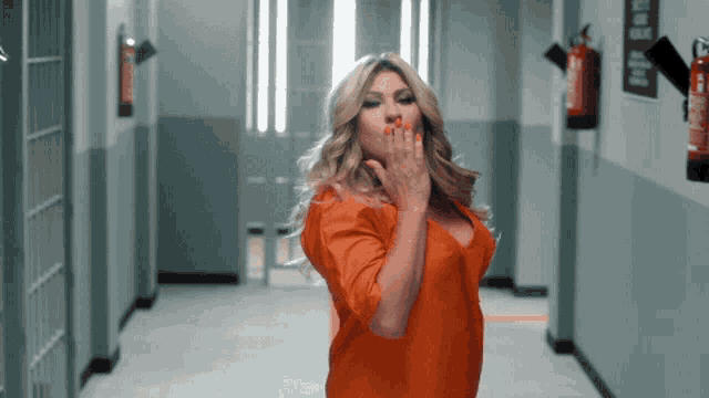 a woman in an orange shirt blows a kiss