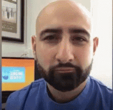 a bald man with a beard wearing a blue shirt looks at the camera .