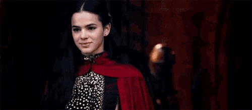 a woman with long black hair is wearing a red cape and a black dress .