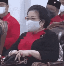 a woman wearing a face mask is sitting in a chair with a purse .