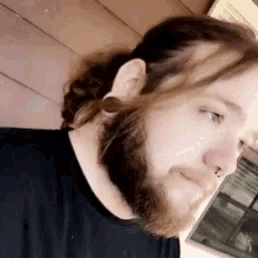 a man with a beard and long hair is wearing a black shirt and earrings .