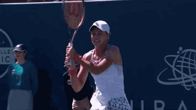 a woman wearing a white hat and a pink wristband is standing on a tennis court .