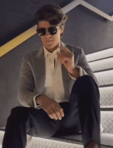 a man in a suit and sunglasses sits on a set of metal stairs