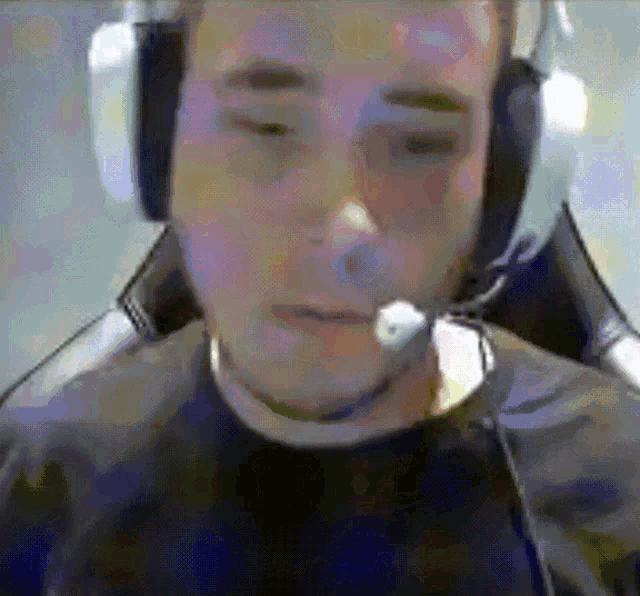 a man wearing headphones and a microphone looks at the camera with his eyes closed