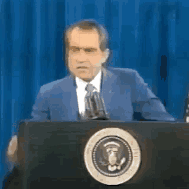 a man in a suit and tie is standing at a podium with a microphone .