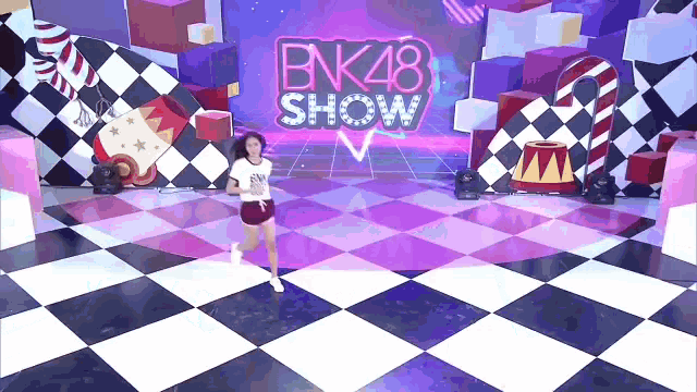 a girl is running on a checkered floor in front of a bnk48 show