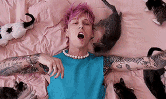 a man with pink hair is laying on a bed with cats around him