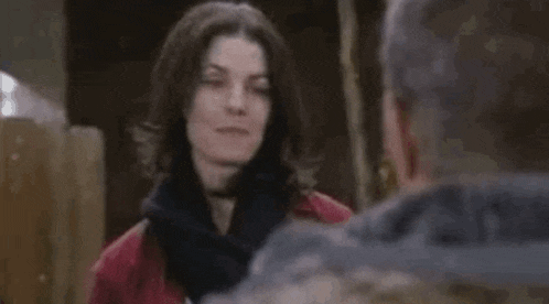a woman in a red jacket and scarf is talking to a man in a gray jacket .