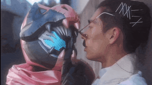 a man is kissing another man 's face while wearing a helmet that says x on it