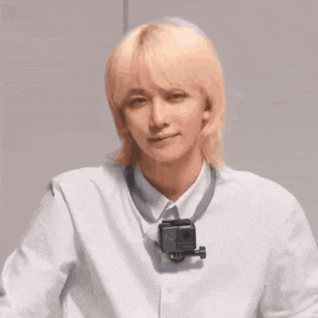 a young man with long blonde hair is wearing a white shirt and a gopro camera around his neck .
