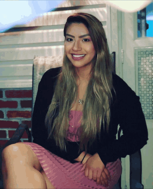 a woman in a pink dress sits in a chair smiling