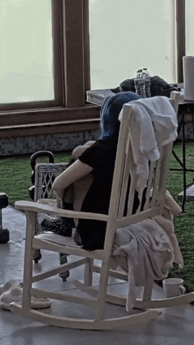 a woman with blue hair sits in a rocking chair with a blanket on the back