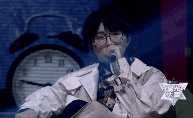 a man with glasses is singing into a microphone in front of a clock