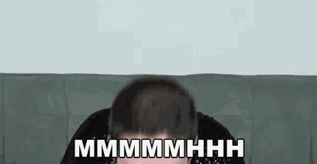 a man is sitting on a couch with his head in his hands and the words `` mmmmmhhh '' written on the screen .