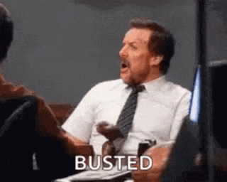 a man in a suit and tie is sitting at a table with his mouth open and the word busted .