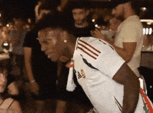 a man in a white adidas shirt is dancing in a crowd of people .