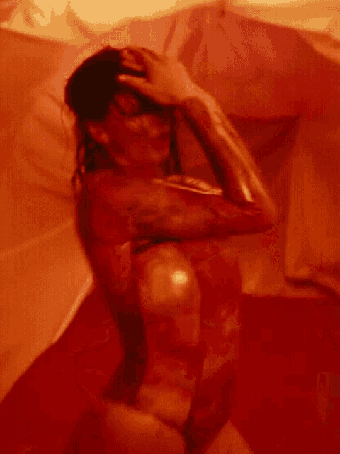 a woman in a red body paint is laying on a bed with her hands on her head .