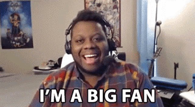 a man wearing headphones and a plaid shirt is laughing and saying `` i 'm a big fan '' .