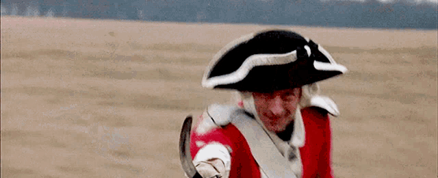 a man in a red uniform and a black and white hat is walking in a field .