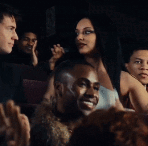 a group of people are sitting in a dark room and a woman is giving a thumbs up
