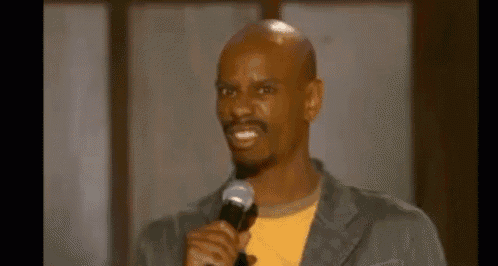 a bald man is holding a microphone and smiling while standing in front of a microphone .