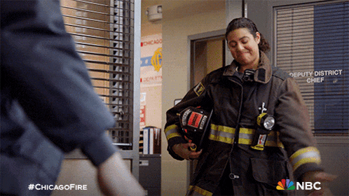 a woman in a fireman 's uniform holds a helmet in front of a door that says deputy district chief on it