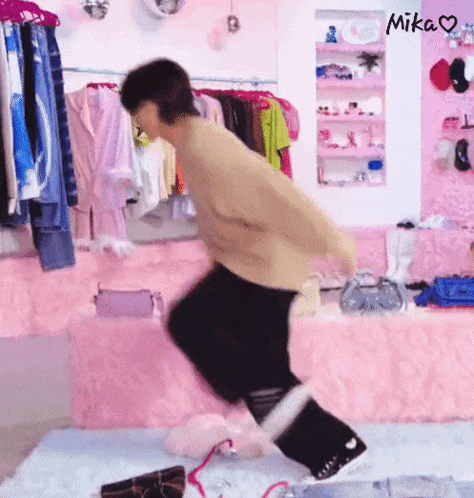 a person is jumping on a pink rug in a room with clothes hanging on the wall .