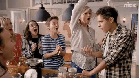 a group of people are standing around a table in a kitchen with their hands in the air .