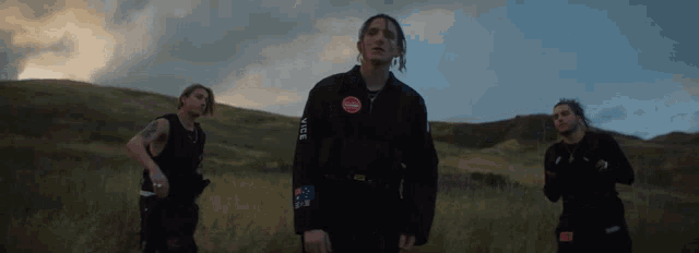 three men are standing in a field with one wearing a jacket that says stop on the front