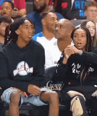 a man and a woman are sitting in the stands at a basketball game wearing all dream team sweatshirts .