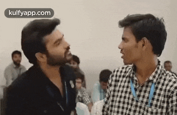 two men are standing next to each other and talking in a room .
