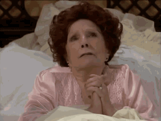 a woman with red hair is laying in a bed with her hands folded in prayer