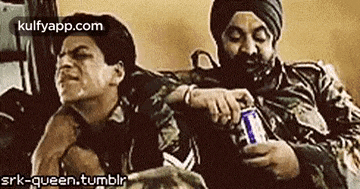 two men are sitting next to each other on a couch . one of the men is holding a can of beer .