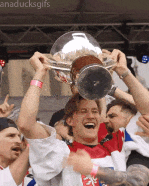 a man in a red shirt is holding a trophy in the air
