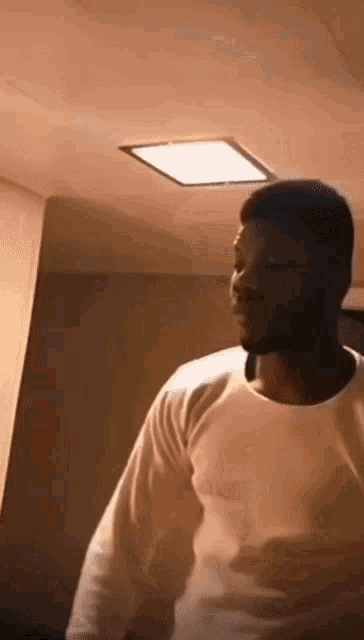 a man in a white shirt is standing in front of a light on the ceiling .