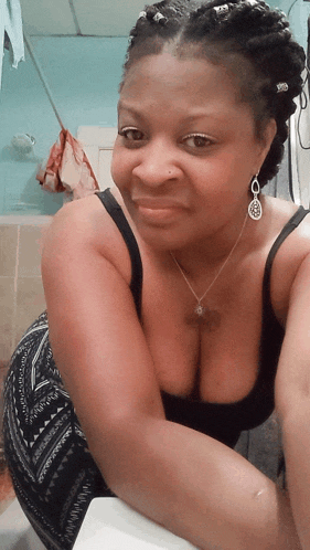 a woman wearing a braided hairstyle and earrings takes a selfie in a bathroom