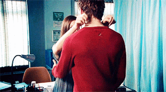 a man in a red sweater is being hugged by a woman in a hospital room