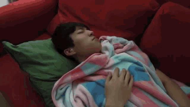 a man is laying on a red couch with a pink and blue blanket on him
