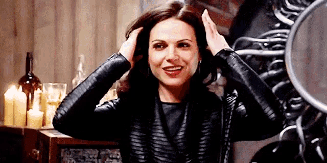 a woman in a leather jacket is smiling while holding her hair in a room .