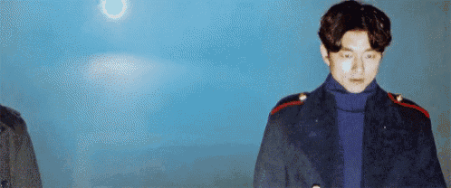 a man in a blue coat and a blue turtleneck is standing in front of a blue sky .