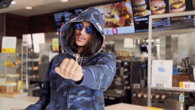 a man wearing a blue hoodie and sunglasses is pointing at the camera in a fast food restaurant .