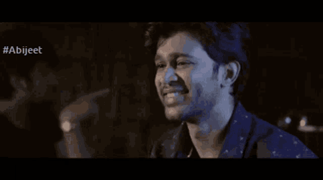 a man in a blue shirt is laughing with his hand on his face .