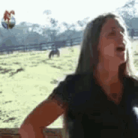 a woman is standing in front of a field with a ball flying in the air .