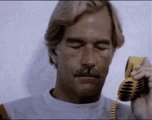 a man with a mustache is talking on a telephone with his eyes closed .